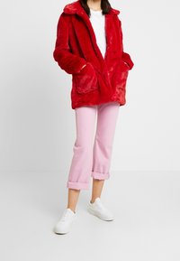 Rød faux pelsjakke med krave og to forlommer, parret med lyserøde cropped jeans og hvide sneakers. Blød tekstur hele vejen igennem.