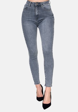 Jean skinny taille haute en denim gris délavé, avec cinq poches, passants de ceinture et fermeture à bouton, associés à des talons hauts noirs.