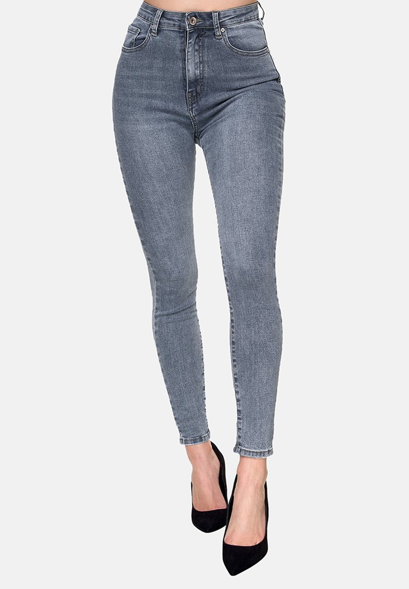 Jeans ajustados de cintura alta en denim gris deslavado, con cinco bolsillos, presillas para cinturón y cierre de botón, combinados con tacones altos negros.