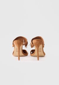 Tan suede high-heeled sandals with an open back, fringe detailing on the sides, and a pointed toe design.