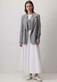 Pilkos juostelės švarkas su atitinkamu liemeniu, derinamas su balta ilga sijonu ir baltais sportbačiais. Švarkas turi dideles atvartus ir kišenes.