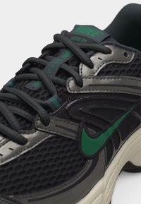 Μαύρο και γκρι αθλητικό παπούτσι Nike Moto 2K με πράσινο λογότυπο swoosh και κορδόνια, με πλέγμα στο πάνω μέρος και επενδεδυμένο γιακά.