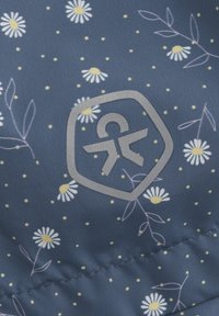 Marinfärgad tyg med gult och vitt blommönster, med små prickar. En silverfärgad logotyp i hexagonform syns på ytan.