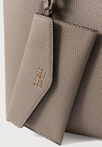 Bolsa de mão de couro texturizado cinza com um porta-cartões destacável, apresentando ferragens douradas embutidas com "GUESS EST 1981."