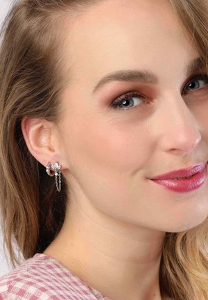 Boucles d'oreilles en argent avec un design en anneau, embellies d'une petite fleur, avec des détails de chaîne et une finition brillante, présentées sur l'oreille d'un modèle.