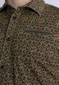Korte mouwen shirt van groene stof met een all-over geometrisch patroon in oranje en zwart. Beschikt over een zwarte zak en knoopsluiting.