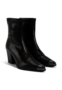 Bottines en cuir noir avec des talons blocs, des bouts pointus et des embouts métalliques. Présente une texture lisse et un design épuré.
