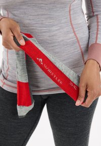 Rote und graue gestreifte Socken, die in der Hand gehalten werden, mit weißem Text auf der Seite, der die Marke "WHISTLER" und die Größe "39-42" angibt. Weiches Material, mittlere Wadenlänge.