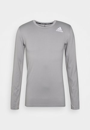 Camiseta deportiva de manga larga en gris claro, hecha de un material suave y ligero. Presenta un pequeño logotipo blanco en la parte superior izquierda del pecho.