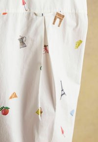 White fabric featuring colorful embroidered motifs, including an Eiffel Tower, bicycle, umbrella, and food items like cheese and croissants.