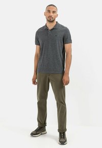 Mørkegrå polo shirt med et struktureret design, korte ærmer og en tre-knaps lukning, parret med olivengrønne bukser og mørke sneakers.