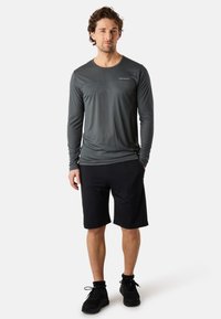 Langärmliges graues Sporthemd mit glatter Textur und dezenter Logodesign, kombiniert mit schwarzen Shorts. Sneaker runden das Outfit ab.