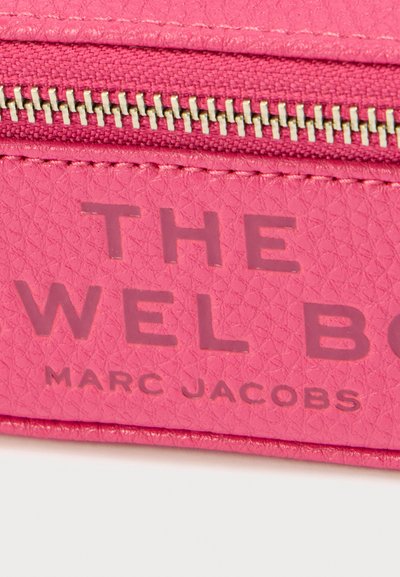 Ροζ καλλυντική θήκη από δερματίνη με υφή, με φερμουάρ, ανάγλυφο όνομα επωνυμίας "THE JEWEL BOX" και "MARC JACOBS" με έντονα γράμματα.