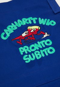Blue fabric featuring embroidered text "CARHARTT WIP" in green and "PRONTO SUBITO" below, with a cartoon character in red with yellow hair.