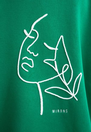 Tissu vert avec un motif brodé blanc représentant un visage et des feuilles, avec le mot "MIRONS" cousu en dessous. Texture lisse et style minimaliste.