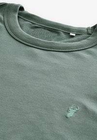 Camisa de algodón verde oliva con cuello redondo, hecha de algodón suave, que presenta un diseño sutil de langosta bordado en el lado izquierdo del pecho.