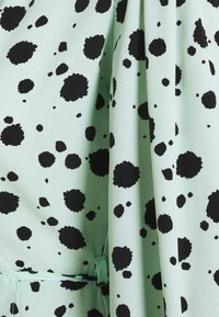 Tissu vert menthe avec des taches d'encre noire. Le matériau est doux, avec une texture lisse, présentant des plis et une ceinture assortie.