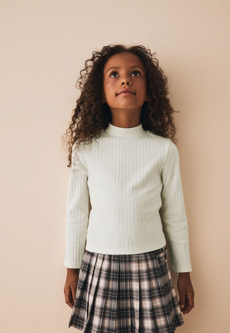 Top de manga larga de canalé en verde claro combinado con una falda de cuadros en tonos negro y beige. El conjunto tiene un diseño ajustado y una textura suave.