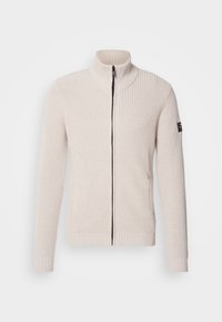 Pull beige en maille avec fermeture éclair, col montant, poignets et ourlet côtelés, et une petite patch noire sur la manche haute gauche.