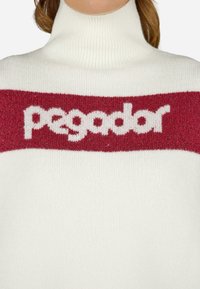 Biały sweter z golfem, ozdobiony czerwoną poziomą taśmą z białym napisem "pegador". Miękka tekstura, żebrowany materiał przy szyi.
