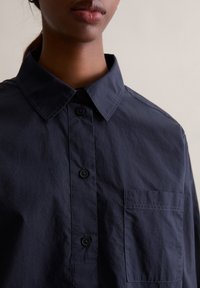 Marineblaue Hemdjacke mit klassischem spitzem Kragen, Brusttasche und leichtem, leicht strukturiertem Stoff.