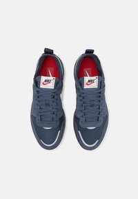 Tenisky Nike s tmavě modrým svrškem z mesh a semiše, červeným vnitřkem, bílými detaily a texturovanými plochými tkaničkami.