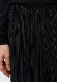 Μαύρη πλισέ φούστα με υφή στην επιφάνεια, με ελαστική μέση με σούρες. Το ύφασμα είναι ε λαφρύ και ρέει ομαλά. Χέρι ορατό στο πλάι.