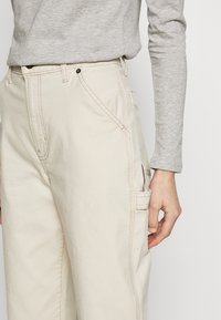 Béžové cargo kalhoty z bavlny, se zřetelným šitím, bočními kapsami a volným střihem. Doplněné šedým dlouhým rukávem.