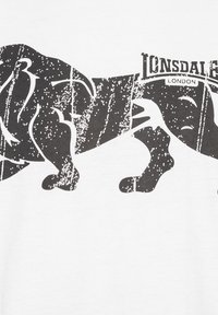 Bílá bavlněná tričko s velkým černým grafickým motivem lva se znehodnocenou texturou, doplněné logem "Lonsdale London" nahoře.