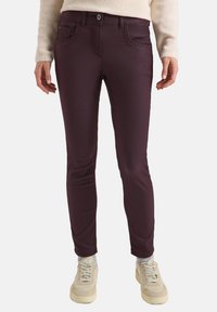 Burgunder, slim-fit jeans med en glat tekstur, der har forlommer og en knaplukning. Sammen med beige sneakers.