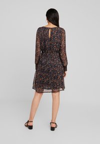 Květinové šaty v tmavě námořnické barvě s oranžovými a bílými vzory, poloprůhledná tkanina, dlouhé rukávy, detail s klíčovou dírkou na zádech a uvolněný střih.