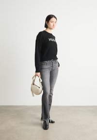 Zwarte trui met de tekst "HUG", grijze flared jeans met een rafelige zoom, zwarte enkellaarsjes en een ronde crèmekleurige handtas. Eenvoudig en modern ontwerp.