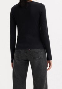 Svart långärmad topp av mjukt tyg, figurnära design, rund halsringning. Matchad med högmidjade mörkgrå jeanstights med dubbla bakfickor.