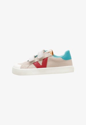 Baskets beiges avec deux brides velcro, logo latéral rouge, talon bleu sarcelle et semelle en caoutchouc blanche.