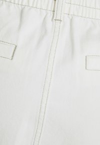 Bílý denimový materiál s prošitými švy, elastickým pasem a dvěma obrysy kapes. Hladký povrch s jemným diagonálním vzorem.