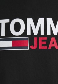 Černé bavlněné tričko s velkým bílým nápisem "TOMMY" a "JEANS", s obdélníkovým detailem loga v červené, bílé a modré barvě.