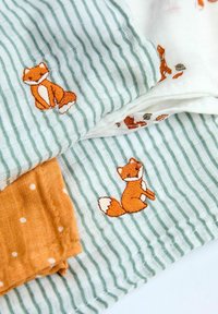 Tre stykker mønstret stof med orange rævbroderi på hvide og grønne stribede baggrunde, samt et ensfarvet sennepsfarvet stykke med hvide prikker.