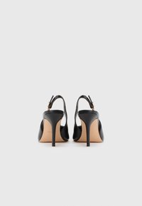 Melni augstpapēžu apavi ar slingback dizainu, gluda ādas tekstūra, mandeles formas pirksti un slaidi papēži. Zelta tonī aksesuāri.