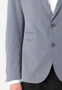 Light blue blazer with a textured fabric, featuring two buttons, a single vent, and a notch lapel. White shirt cuff visible.