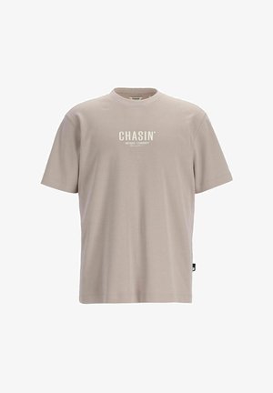 Camiseta de algodón beige con mangas cortas y cuello redondo. Presenta el logo "CHASIN'" en blanco en la parte delantera. Textura suave y corte relajado.