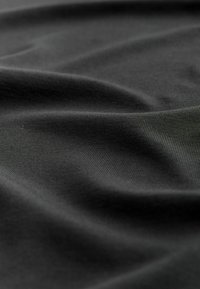 Tessuto di cotone nero con una texture liscia, che mostra leggere pieghe e grinze, creando un aspetto morbido e stratificato.