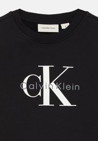 Čierna mikina so širokým bielym logom "CK" a menším textom "Calvin Klein". Pružný výstrih a manžety, vyrobená z materiálu z bavlny.