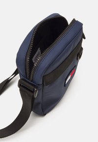 Bolso bandolera navy con cierre de cremallera, correa negra y parche de marca. Fabricado con un tejido duradero de textura suave.