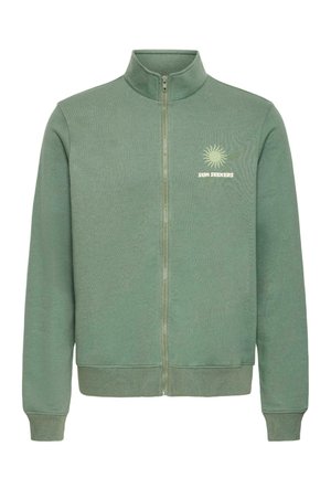 Sweat-shirt à fermeture éclair vert avec col montant, poignets et ourlet côtelés, et un motif de soleil jaune avec le texte "SUN SEEKERS" sur la poitrine gauche.