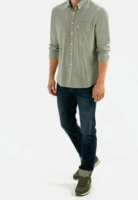 Camisa de cuadros verde y blanca con botones y mangas largas, combinada con jeans azul oscuros y zapatillas verdes. Atuendo casual con diseño sencillo.