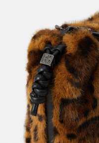Brun kunstpelsveske med leopardmønster, som har svarte lærdetaljer, et flettet stropp og en metallisk logoetikett.