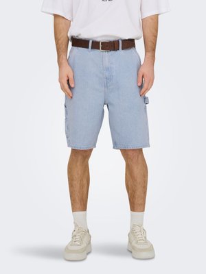 Homme portant un short cargo en denim bleu clair, des chaussettes blanches montantes, des baskets beiges, un t-shirt blanc et une ceinture en cuir marron.
