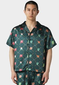 Camisa verde de manga corta hecha de tejido satinado, con patrones florales en rosa, naranja y verde, con un cierre de botones en la parte delantera y un corte relajado.