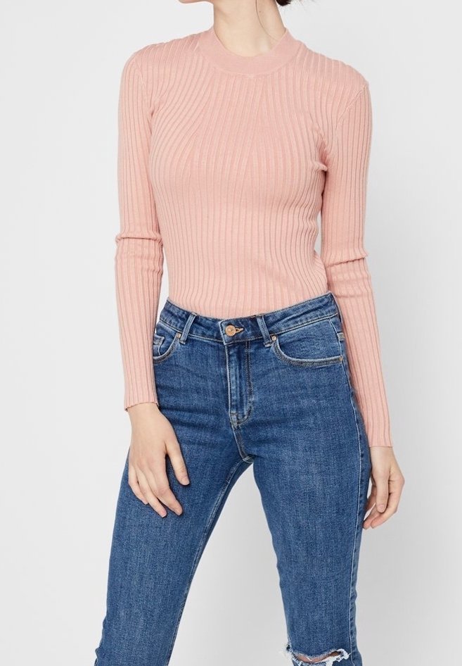 Personne portant un pull à manches longues rose côtelé, rentré dans un jean en denim bleu taille haute avec un genou déchiré.