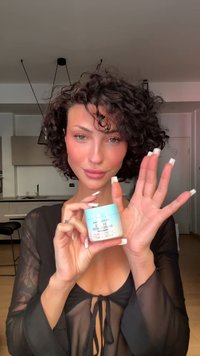 Hvit krukke med lys blå lokk, merket "Revolution" og "Bamboo Powder." Modell i svart gjennomsiktig topp holder krukken, som viser produktdetaljene.